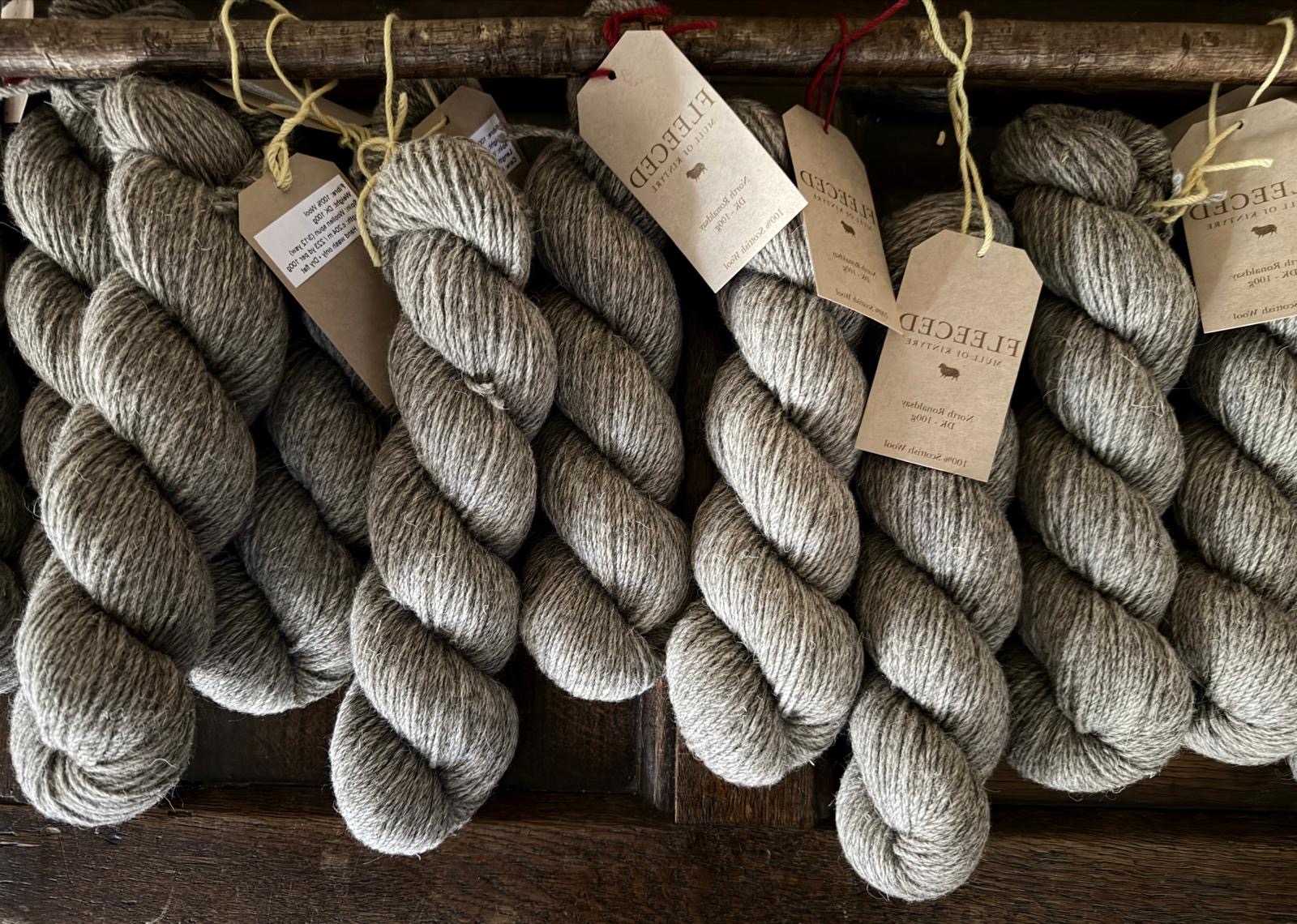 Fleeced skeins of North Ronaldsay wool hanging on a wooden rack, brand tags attached